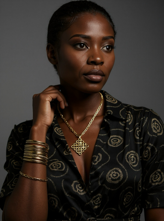 Model wearing the gold-tone Bela 2.0 Ethiopian cross necklace with a dark patterned blouse