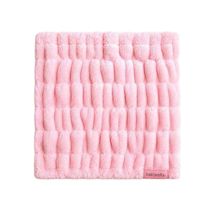 Pink Hairbrella spa headband laid flat, showing its wide gathered microfiber side and small logo label.