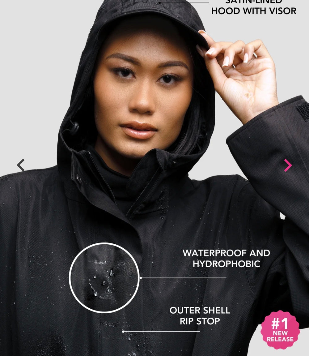 Model wearing a black Hairbrella rain jacket with the hood up; callouts identify the satin-lined visor hood and waterproof ripstop shell.