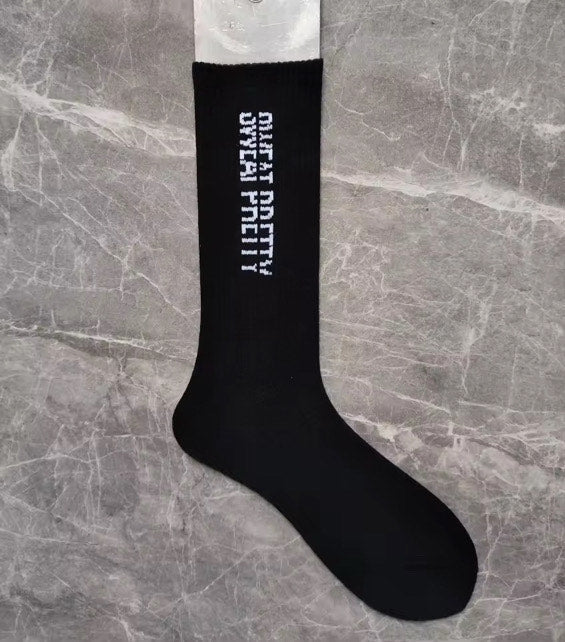 Black Sweat Pretty sock with vertical white lettering, displayed on a foot form against gray marble.