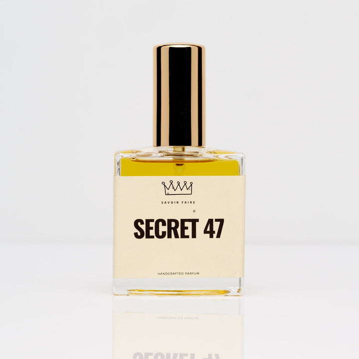 Savoir Faire Secret 47 perfume in a rectangular clear bottle with golden liquid, a cream label and tall gold-tone cap.